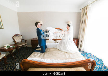 Portrait of happy smiling newlywed couple fighting with pillows on bed in hotel room Stock Photo