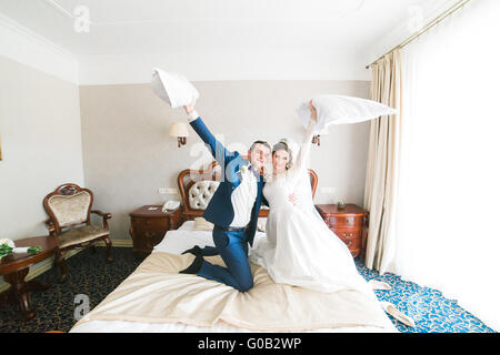 Portrait of happy smiling newlywed couple fighting with pillows on bed in hotel room Stock Photo