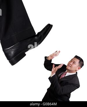 Business concept image of an Asian businessman holding on under pressure of big boss, under giant shoe, isolated on white Stock Photo