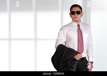 Young and proud Asian businessman wearing black glasses holding his jacket suit on his arm over bright background Stock Photo
