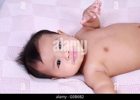 Portrait of cute little Asian baby girl lying down on bed and smiling to the camera Stock Photo