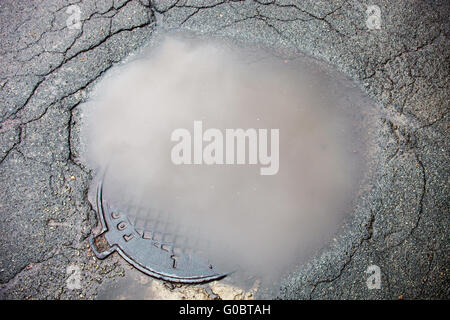 The puddle on the manhole in asphalt surface Stock Photo