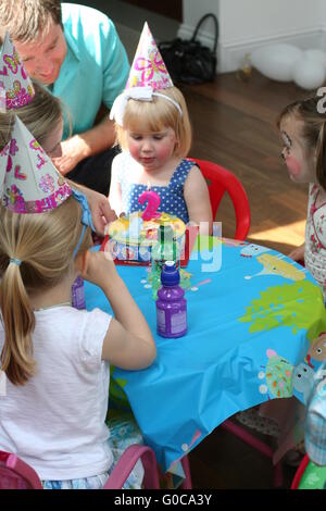Childrens /Kids birthday party, Children sitting around party table  two year old wearing face paint party hats pigtails, family fun, party concept Stock Photo