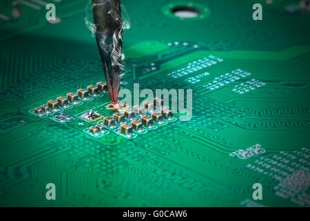 smoking soldering iron on a computer motherboard closeup Stock Photo
