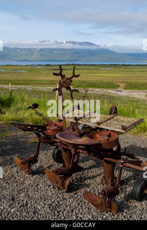 Iceland, Akureyri. Historic turf houses of Laufas. Vintage farm  equipment with scenic fjord in the distance. Stock Photo