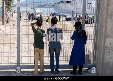 Three refugees from Syria watch a departing ferry leaving from the island of Lesvos to Athens, Greece. Stock Photo