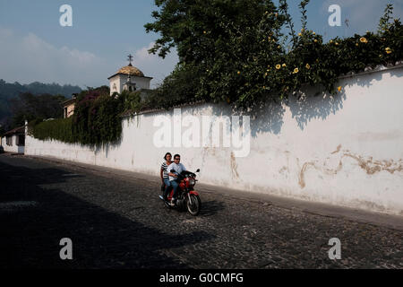 Locals riding a scooter in Antigua a city in the central highlands of Guatemala famous for its well-preserved Spanish Baroque-influenced architecture and a UNESCO World Heritage Site. Stock Photo
