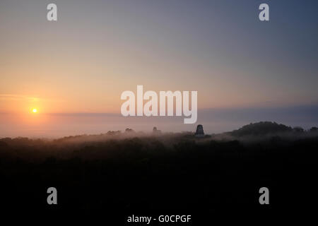 Sunrise and early morning mist over the tropical jungle as seen from the ancient Mayan temple number 4 at the archaeological site of Tikal an ancient urban center of the pre-Columbian Maya civilization located in the archaeological region of the Peten Basin in northern Guatemala Stock Photo