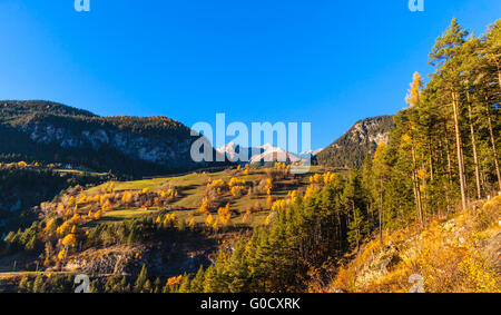 Panorama view of swiss countryside in Filisur, Canton of Grisons, with colorful trees and the Alps in golden autumn at dusk. Stock Photo