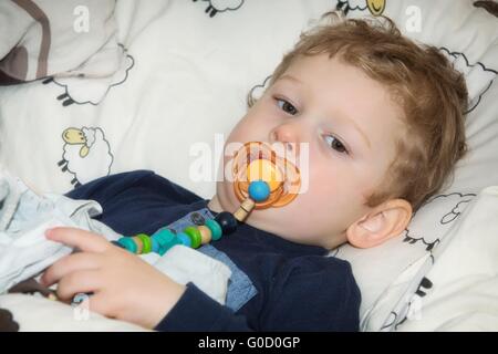 2-year-old boy with pacifier before falling asleep in bed Stock Photo