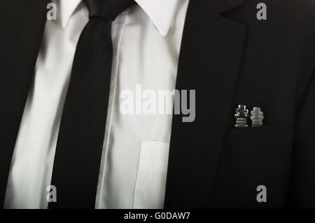 Closeup black suit jacket chest pocket with glass chess pieces sitting inside, white shirt and tie visible Stock Photo
