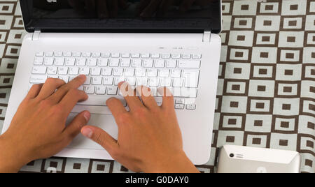 White laptop as seen from above with hands typing on keyboard Stock Photo