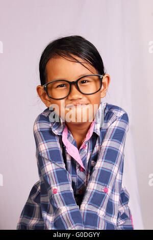 Cute Little girl with glasses performing tight lipped smile while closing her shoulders Stock Photo