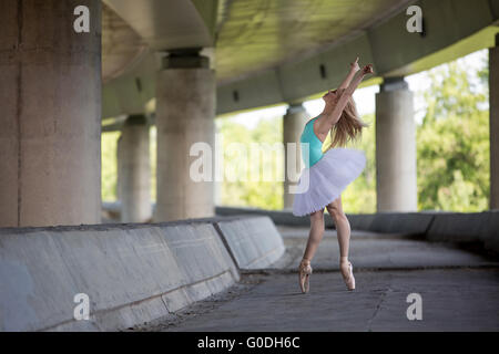 Graceful ballerina doing dance exercises on a concrete bridge Stock Photo