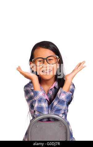 Cute little girl with glasses sitting backward on chair smiling and showing hurray gesture isolated on white Stock Photo