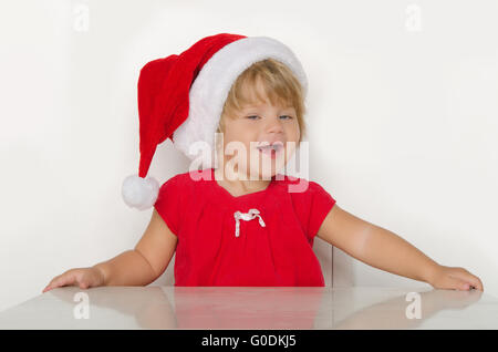 girl in costume of Santa Claus at table and smiling Stock Photo