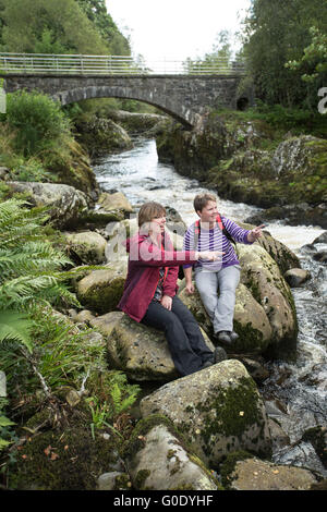 Two women hikers take a rest by waterfall and bridge in Glentrool Stock Photo