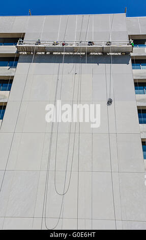 A suspended Scaffolding platform high above the street on a high rise building with men working to clean the building Stock Photo