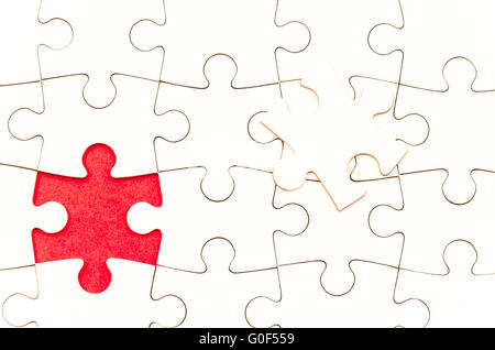 still life with a white jigsaw/puzzle incomplete over a red background, the last piece is over the other one, symbol of problem Stock Photo