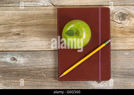Leather notepad with apple and pencil for school or office on rustic wooden boards Stock Photo