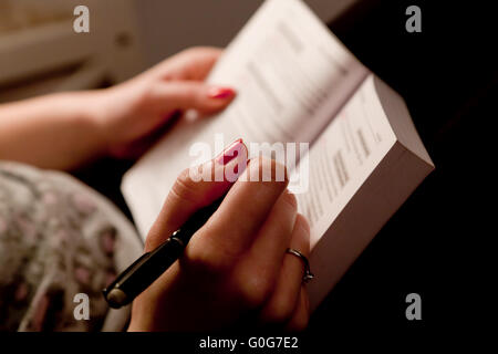 Close-up of a woman hands taking notes in a book while studying at home lying on bed Stock Photo