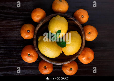 Lemons in wooden plate with mandarines and mint leafs on dark background close-up macro Stock Photo