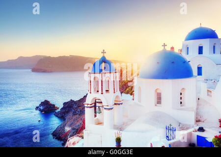 Oia town on Santorini Greece at sunset. Traditional and famous white houses and churches with blue domes over the Caldera Stock Photo