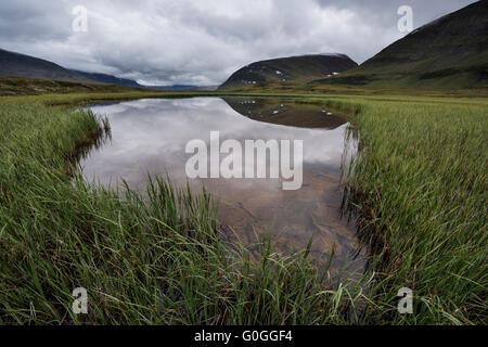 Reflection of mountain landscape of Tjäktjavagge valley in small pond near Sälka hut; Kungsleden trail; Lapland; Sweden Stock Photo