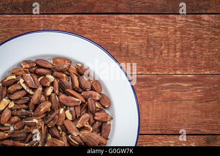 roasted pili nuts grown in Philippines, top view of nuts on white metal plate against  a rustic abrn wood Stock Photo