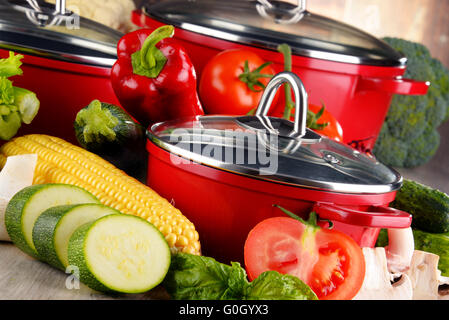 Composition with red steel pots and variety of fresh vegetables. Stock Photo