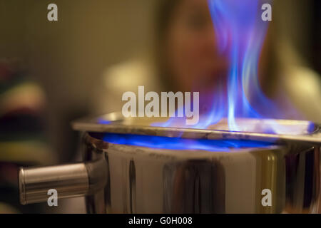 An elderly lady sitting with a surprised face behind the blue flame of a fire tongs punch. Stock Photo