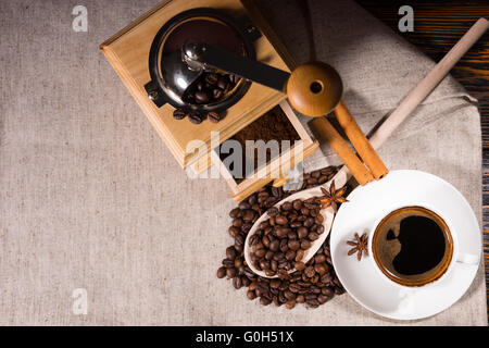 Grinder with coffee beans and wooden spoon beside mug decorated with star anise and cinnamon sticks on canvas Stock Photo
