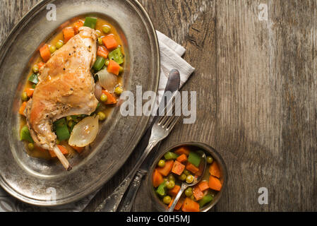 Roast rabbit leg with stewed vegetables on wooden table. Stock Photo