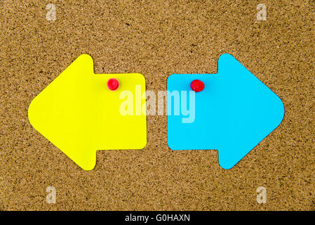 Blank yellow and blue paper notes in shape of opposite arrows pinned on cork board with thumbtacks, copy space available Stock Photo