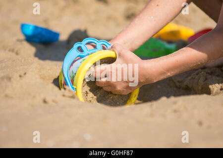 The baby is gaining a bucket in the wet sand, close-up Stock Photo