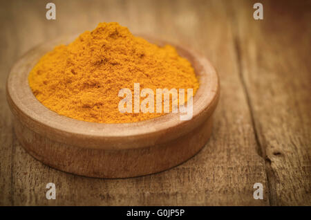 Ground turmeric in a bowl on wooden surface Stock Photo