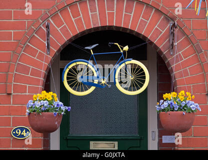 Great Ayton, North Yorkshire UK, 1 May 2016. Many properties in the village are decorated in honour of the cycling Tour de Yorkshire, stage 3 of which passes through the village today. At this address, a painted bike hangs above the front door, with flower-filled hanging baskets in the official Yorkshire colours on either side. Stock Photo