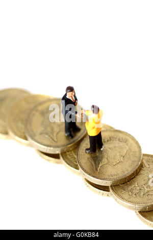 Miniature businessmen shaking hands on pound coins Stock Photo