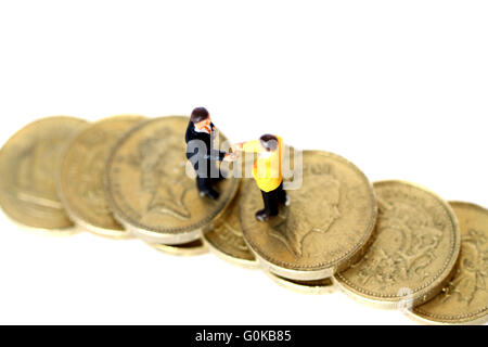 Miniature businessmen shaking hands on pound coins Stock Photo