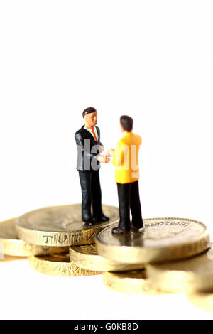 Miniature businessmen shaking hands on pound coins Stock Photo