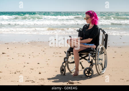 Disabled woman using mobile phone at the beach on a bright day Stock Photo
