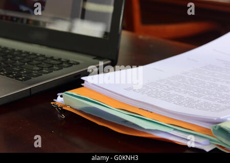 Laptop with stack of folders on table Stock Photo