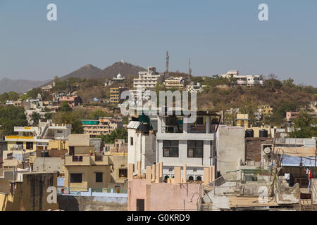 A high view over rooftops in Udaipur during the day. The outside of buildings and hills can be seen. Stock Photo