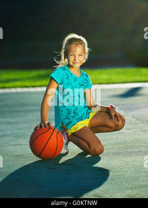 photo of little cute girl playing basketball outdoors Stock Photo