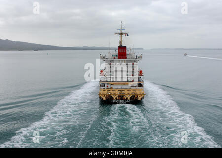Container ship Southern Lily heads out of Auckland Harbour with shipping containers and cars on deck. Stock Photo