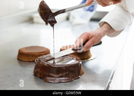 pastry chef covering cake with melted chocolate Stock Photo