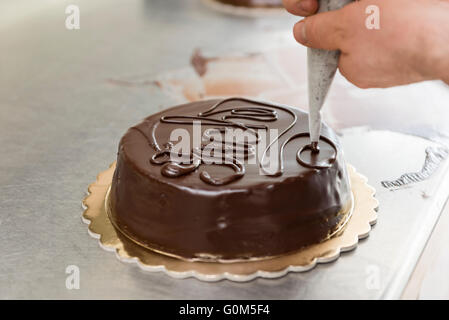 pastry chef garnish a cake with melted chocolate Stock Photo