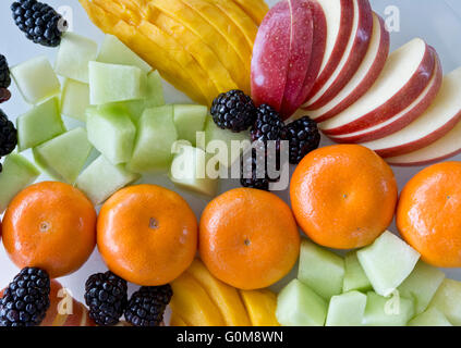 Colourful mixed fruit plate with sliced apples mangoes honeydew melon cubes blackberries and tangerines.  View from above. Stock Photo