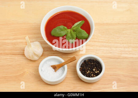 Tomato passata in a bowl with basil, garlic and salt and pepper on a wooden chopping board Stock Photo