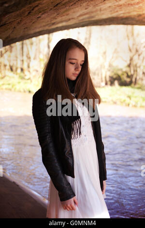 Pretty teenage girl standing under a bridge with a river in the background Stock Photo